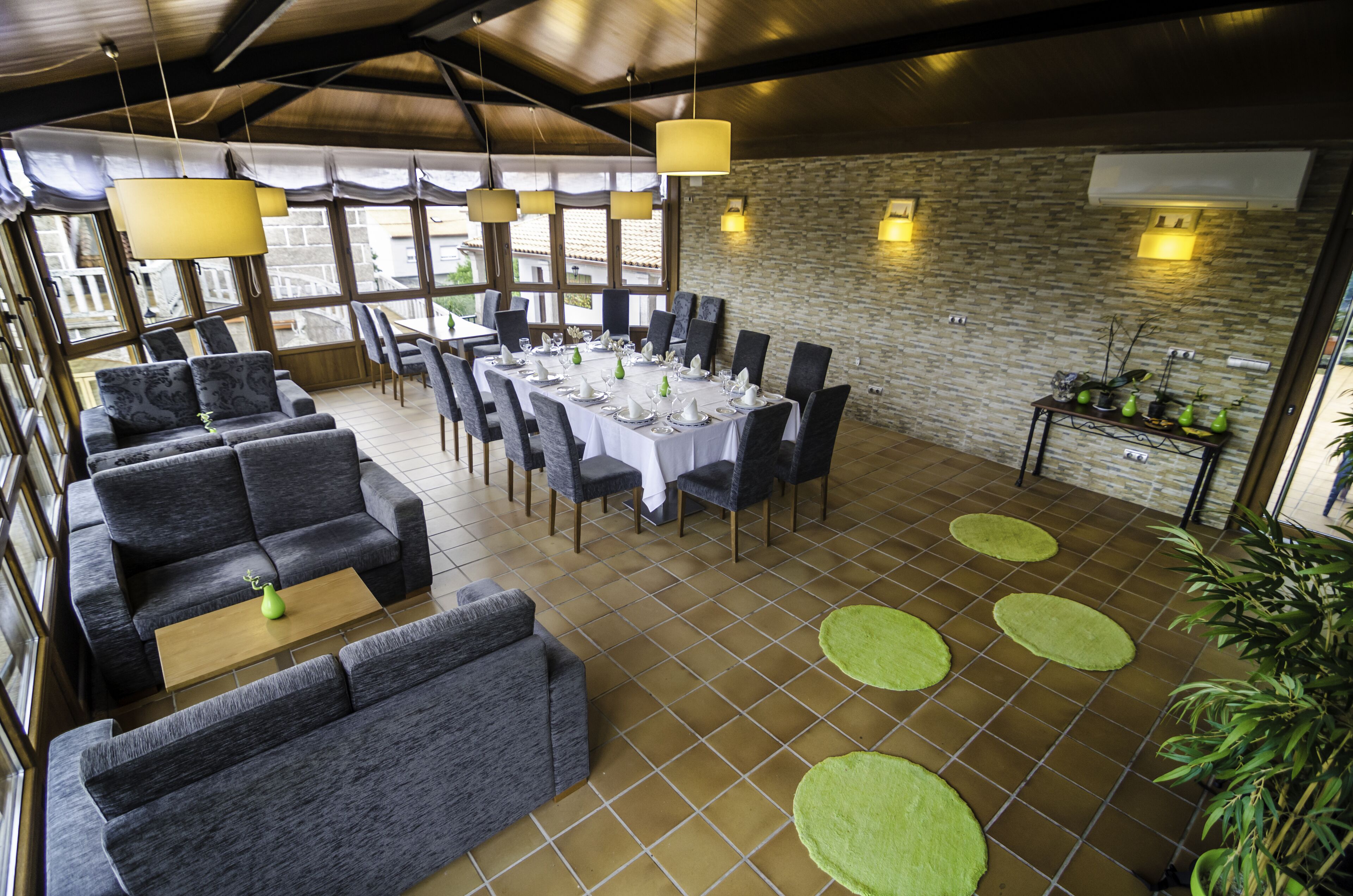 En restaurant med et langt spisebord dækket til et måltid, omgivet af grå sofaer og stole.