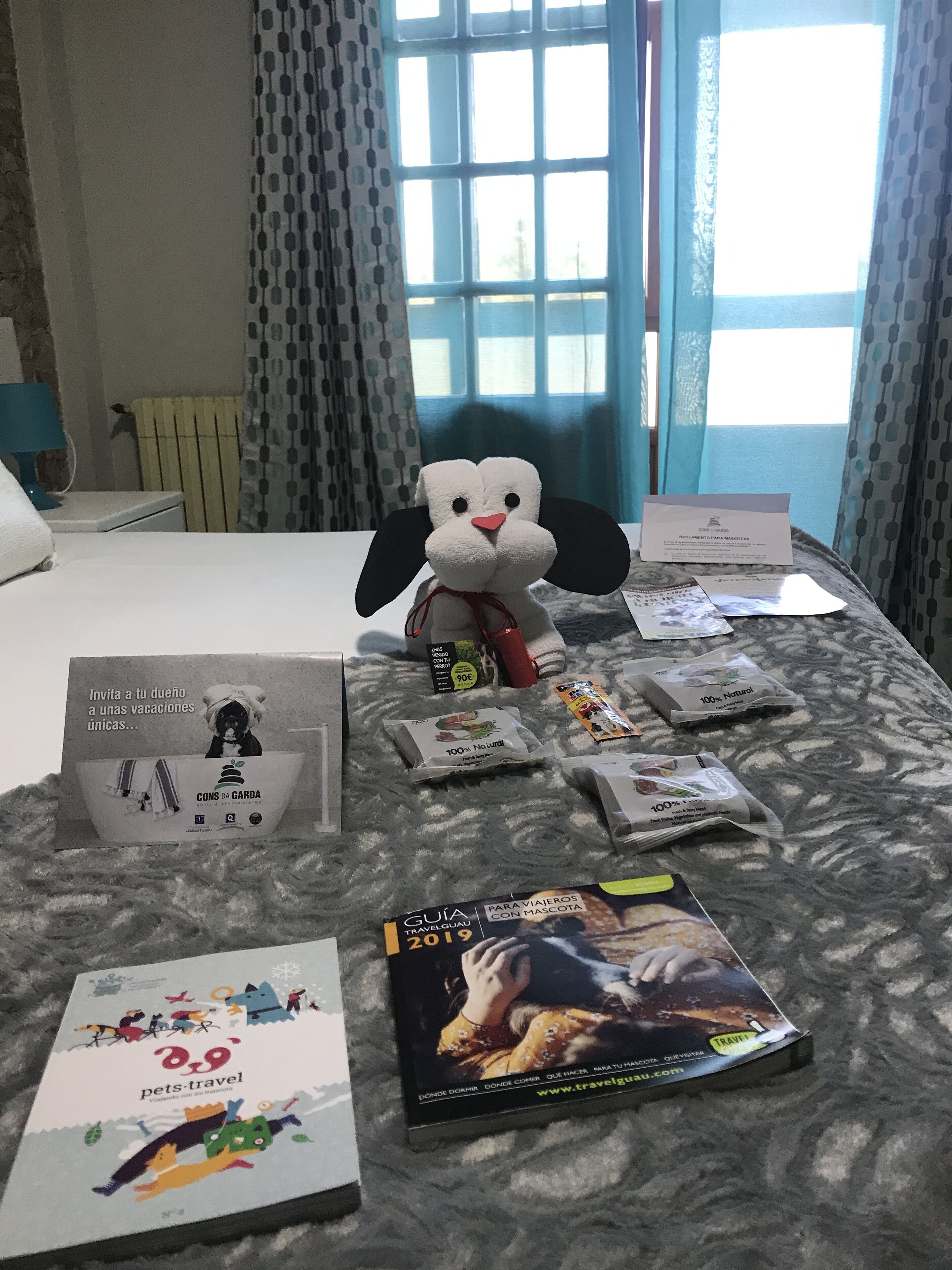 A hotel room with a bed, a plush toy, travel brochures, and a sign indicating pet-friendly policies.