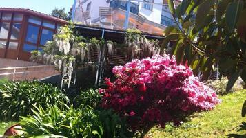 En bygning med balkon og have med lyserøde blomster.