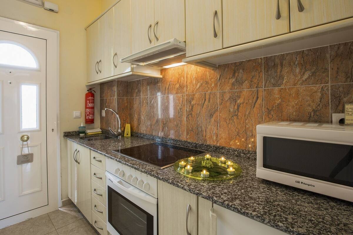 A kitchen with white cabinets, a granite countertop, a stove, a microwave, and a sink with a faucet.