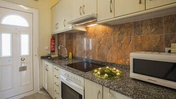 A kitchen with white cabinets, a granite countertop, a stove, a microwave, and a sink with a faucet.