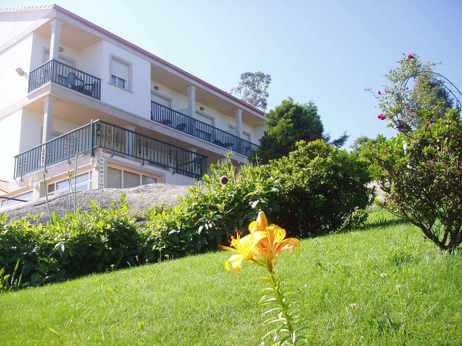 A building with a balcony, surrounded by greenery and a single yellow flower in the foreground.