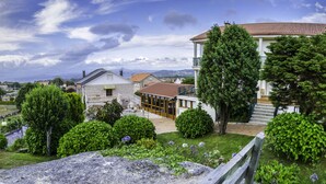 A traditional building with a balcony, surrounded by lush greenery and a stone pathway. - Hotel & Apartamentos Cons da Garda (O Grove)