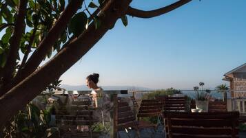 Una terraza con sillas y mesas de madera, con vista a una masa de agua y montañas distantes.