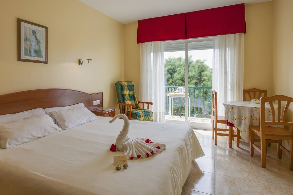 A hotel room with a bed, a chair, a table, and a balcony with a view.