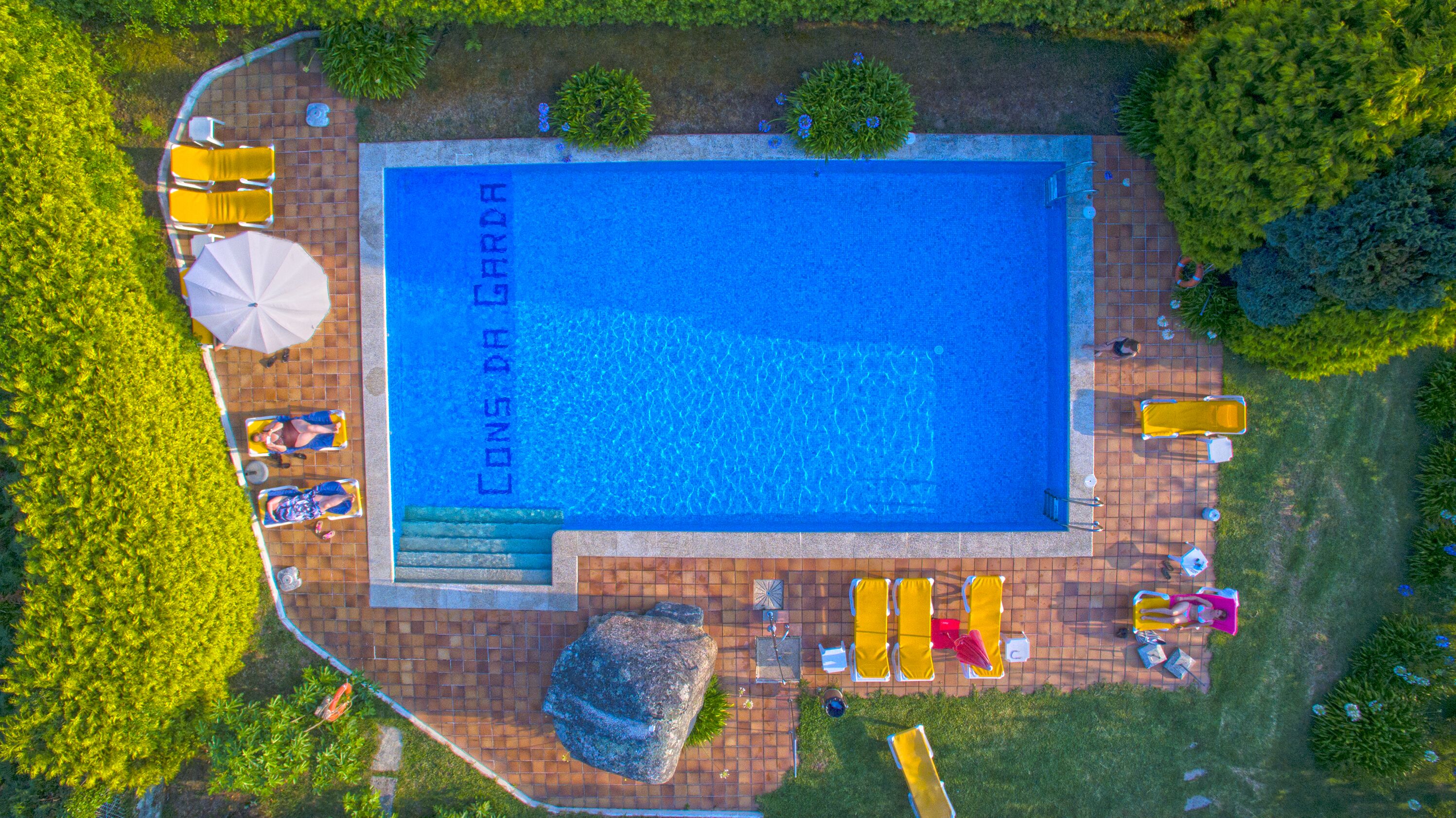 An aerial view of a rectangular swimming pool with a tiled deck surrounding it.