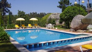 A swimming pool with yellow and white lounge chairs, surrounded by greenery and a large rock. - Hotel & Apartamentos Cons da Garda (O Grove)
