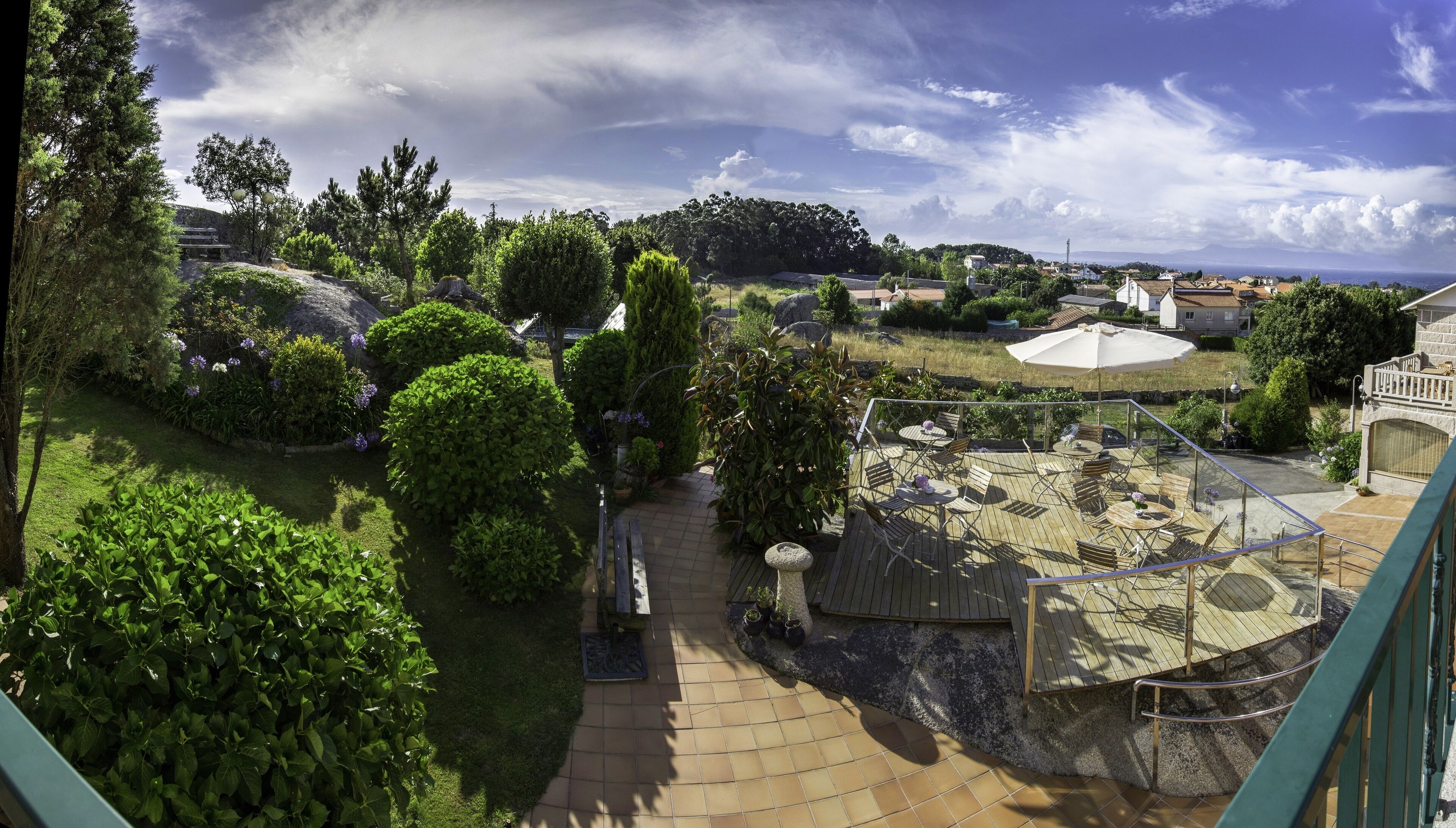 Un jardín con terraza de madera, sendero de piedra y diversas plantas.