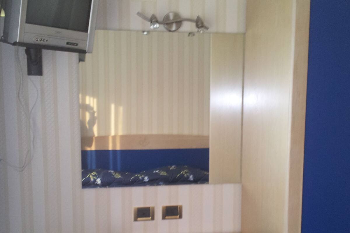 A compact room with a desk, a chair, a television mounted on the wall, and a cabinet.