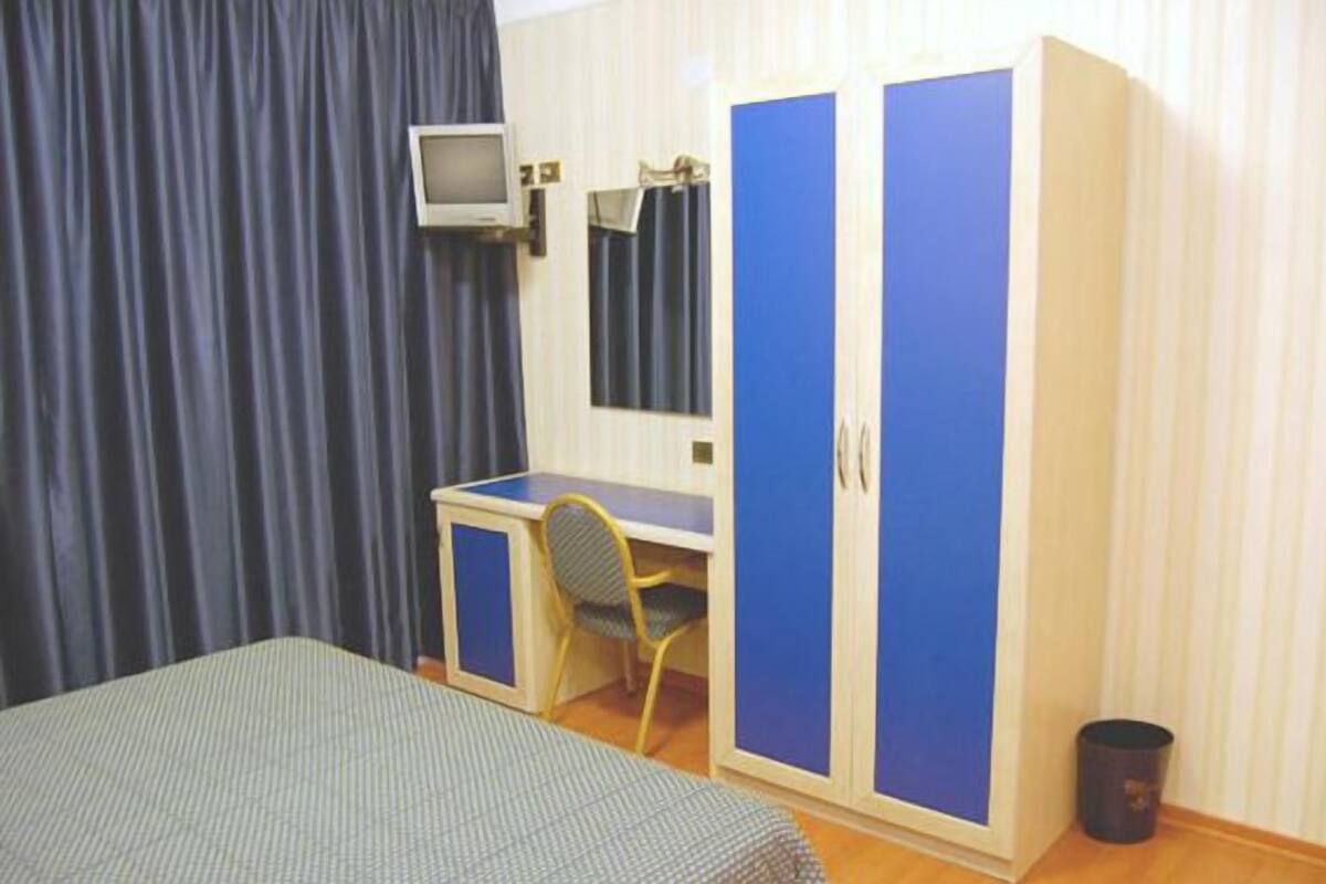 A bedroom with a bed, a desk, and a wardrobe.