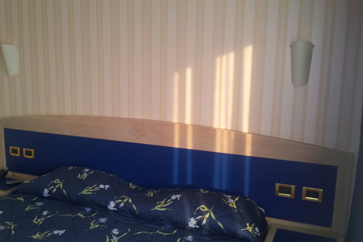 A bedroom with a striped wallpaper, a wooden headboard, a floral bedspread, and a bedside table with a lamp.