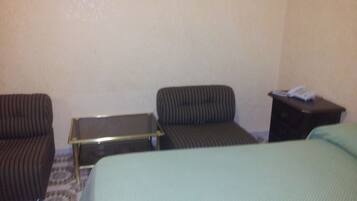 A hotel room with a bed, two chairs, a small table, and a nightstand with a telephone.