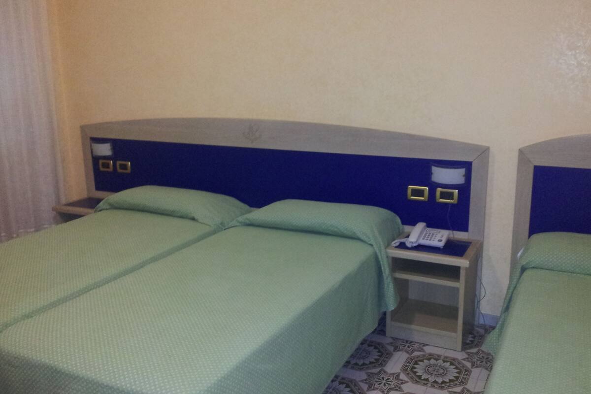 A hotel room with two single beds, a bedside table with a phone, and a small cabinet.