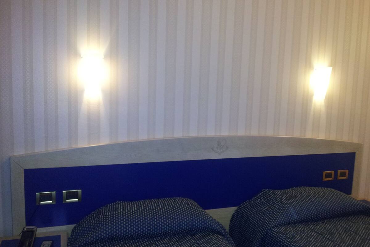 A hotel room with a large bed, two bedside tables, and a headboard with a crest emblem.