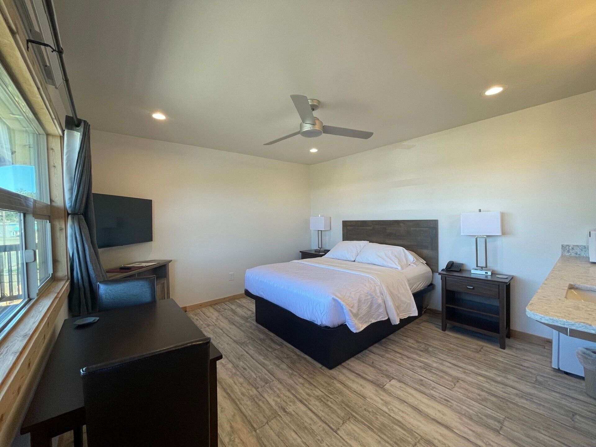 A modern hotel room with a bed, bedside tables, a desk, and a ceiling fan.
