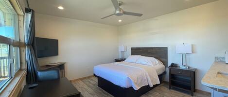 Una habitación de hotel moderna con cama, mesitas de noche, escritorio y ventilador de techo.