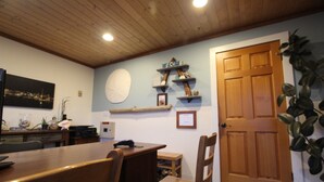 A dining area with a wooden table and chairs, a wall-mounted shelf with decorative items, a door, and a plant. - The Inn at Old Town (Bandon)