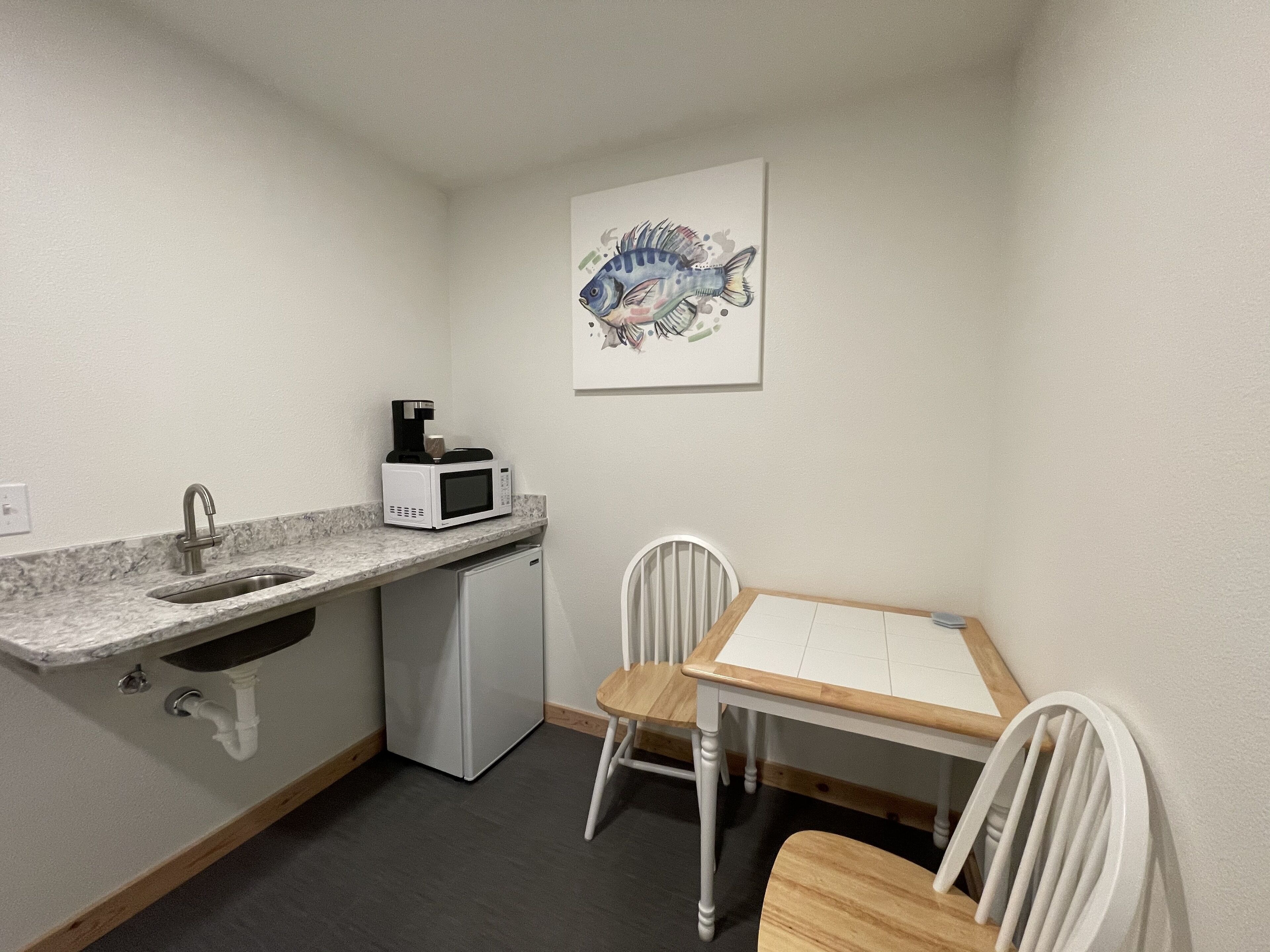 A compact kitchen with a sink, a microwave, a small refrigerator, and a dining table with chairs.