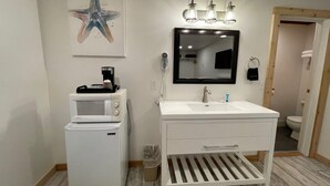 A modern bathroom with a white sink, a mirror, a coffee maker, and a trash can. - The Inn at Old Town (Bandon)