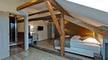 A bedroom with a sloped ceiling, wooden beams, a bed, a desk, and a chair.