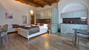 Un dormitorio con techo de madera, una cama, una silla, una mesita y una kitchenette.