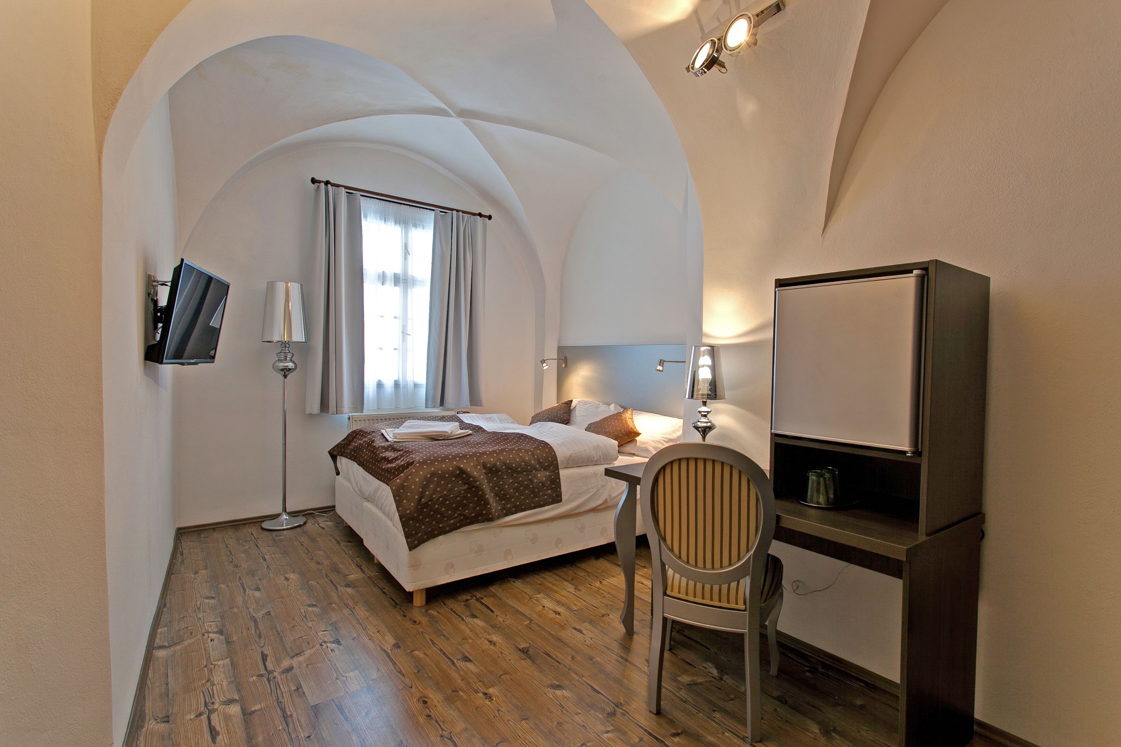 Un dormitorio con cama, escritorio, silla, televisor y lámpara.