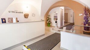 Zona de recepción con un mostrador blanco, un cartel que dice "U Tří hrušek" y un jarrón decorativo con flores.