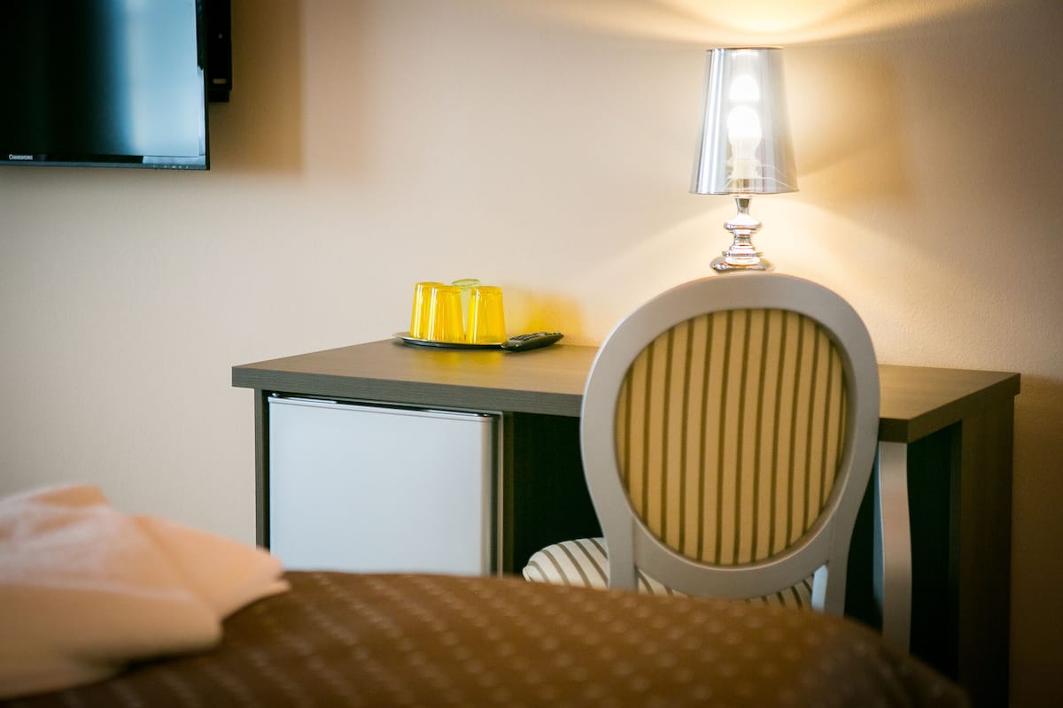 A hotel room with a bed, a desk with a lamp, and a television on the wall.
