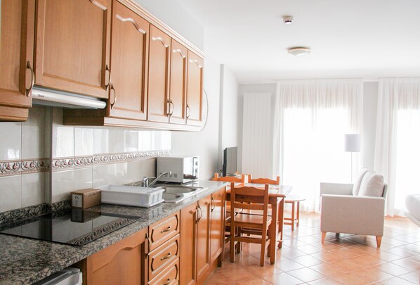 A modern kitchen with wooden cabinets, a granite countertop, and a dining area with a table and chairs. - Apartamentos Soldeu Luxury 3000 (Bordes d'Envalira)