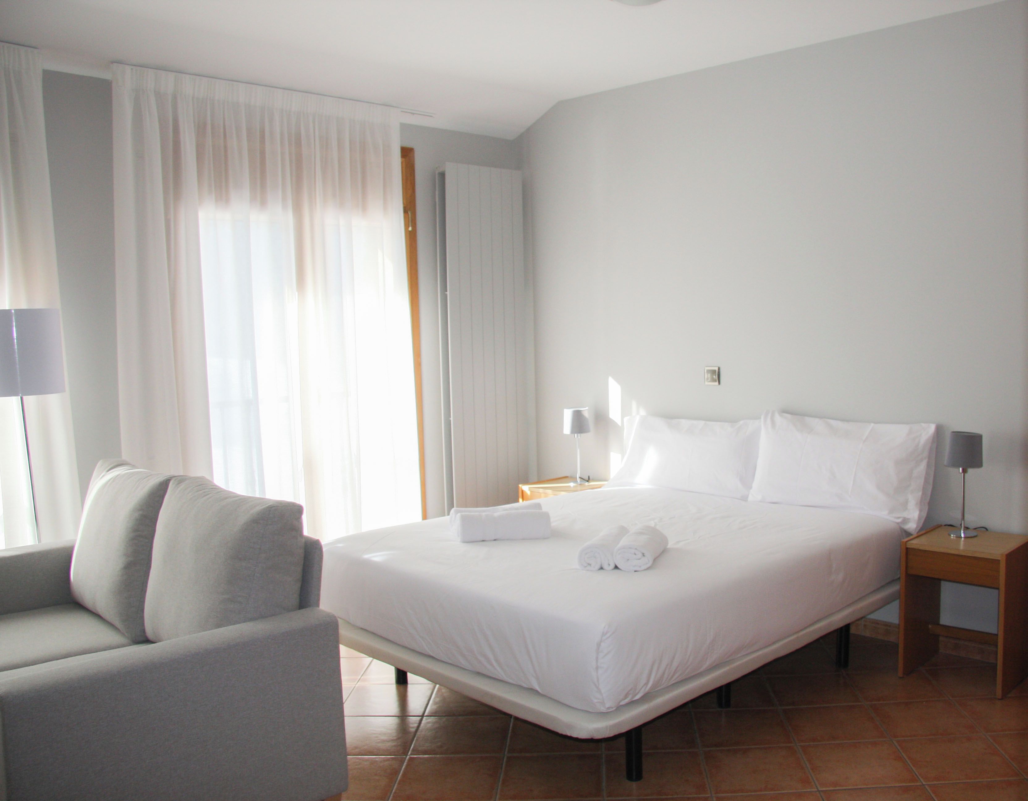 A hotel room with a bed, a chair, a nightstand, and a lamp.