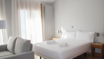 A hotel room with a bed, a chair, a nightstand, and a lamp.