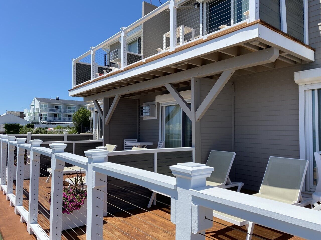A deck with white railings, a wooden floor, and white lounge chairs.