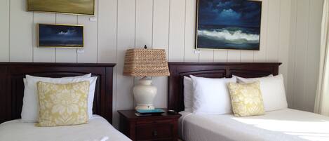 A hotel room with two beds, a nightstand, a lamp, and two paintings of landscapes.