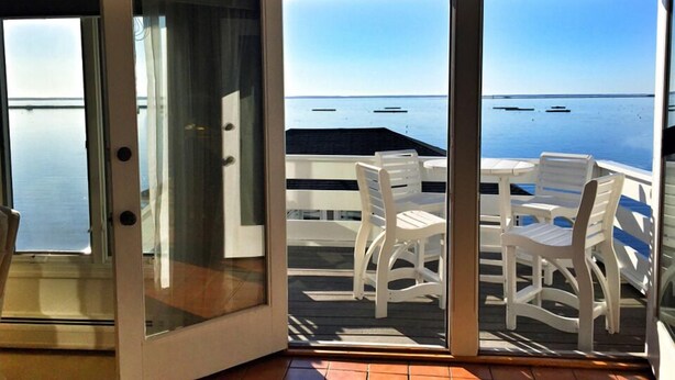 A room with a sliding glass door leading to an outdoor deck with white plastic chairs and a table.
