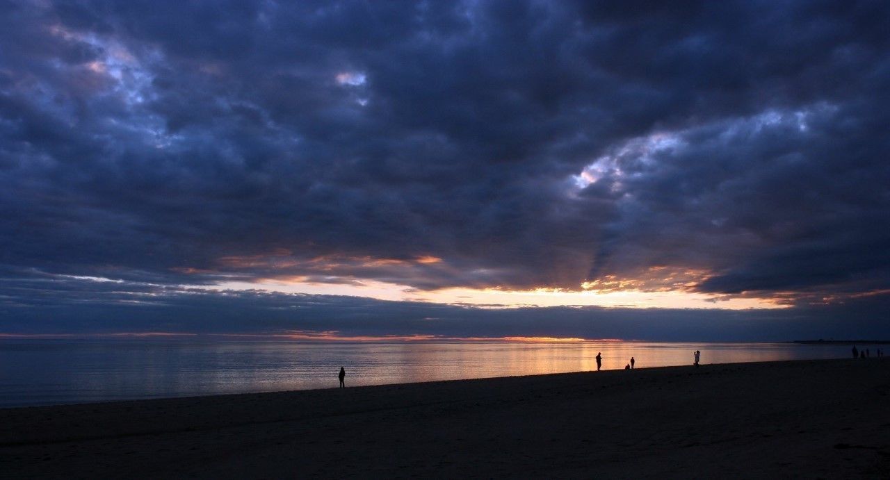 En strand med en solnedgång, silhuetter av människor och ett lugnt hav.