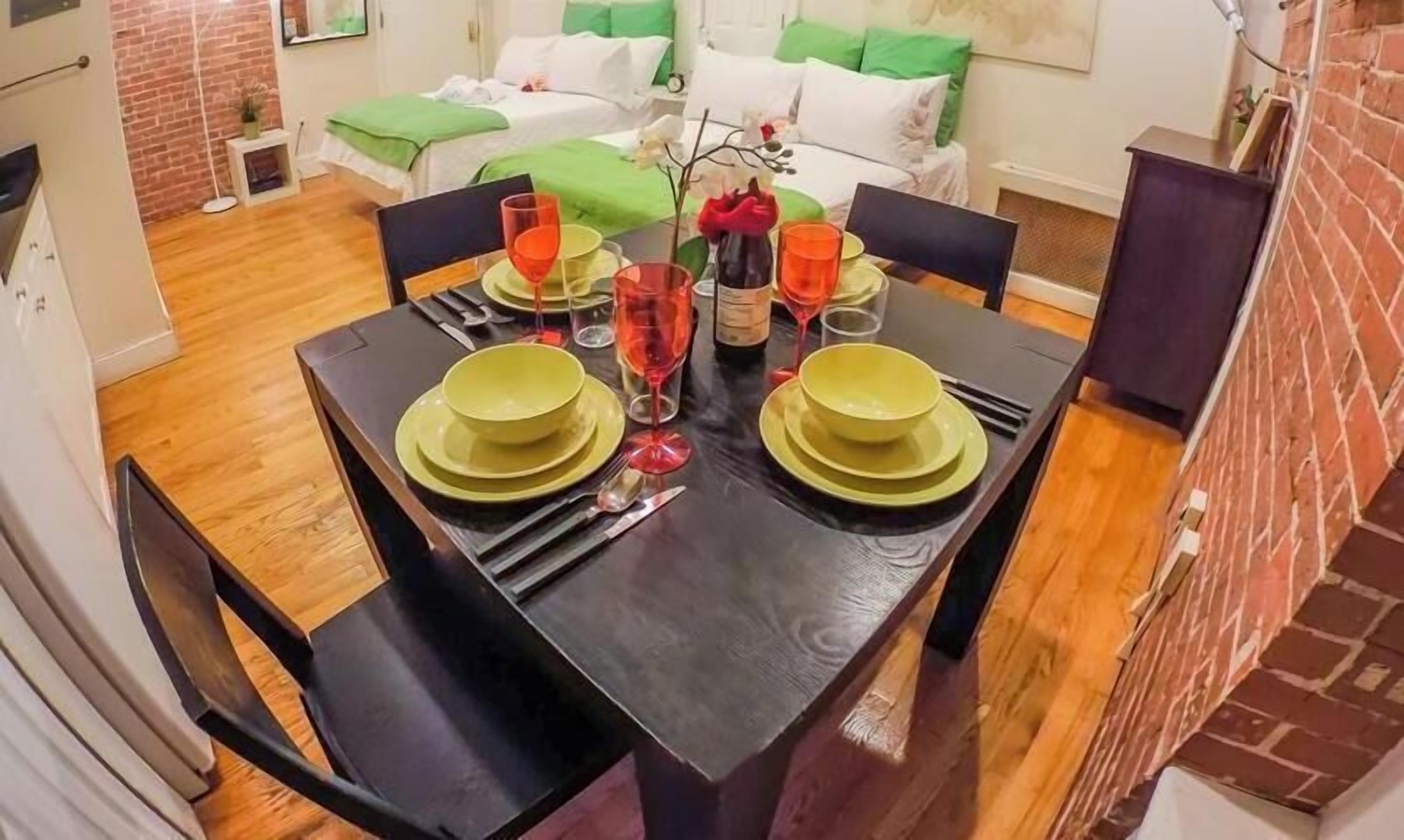 A dining area with a wooden table set for two, featuring green plates and red wine glasses.