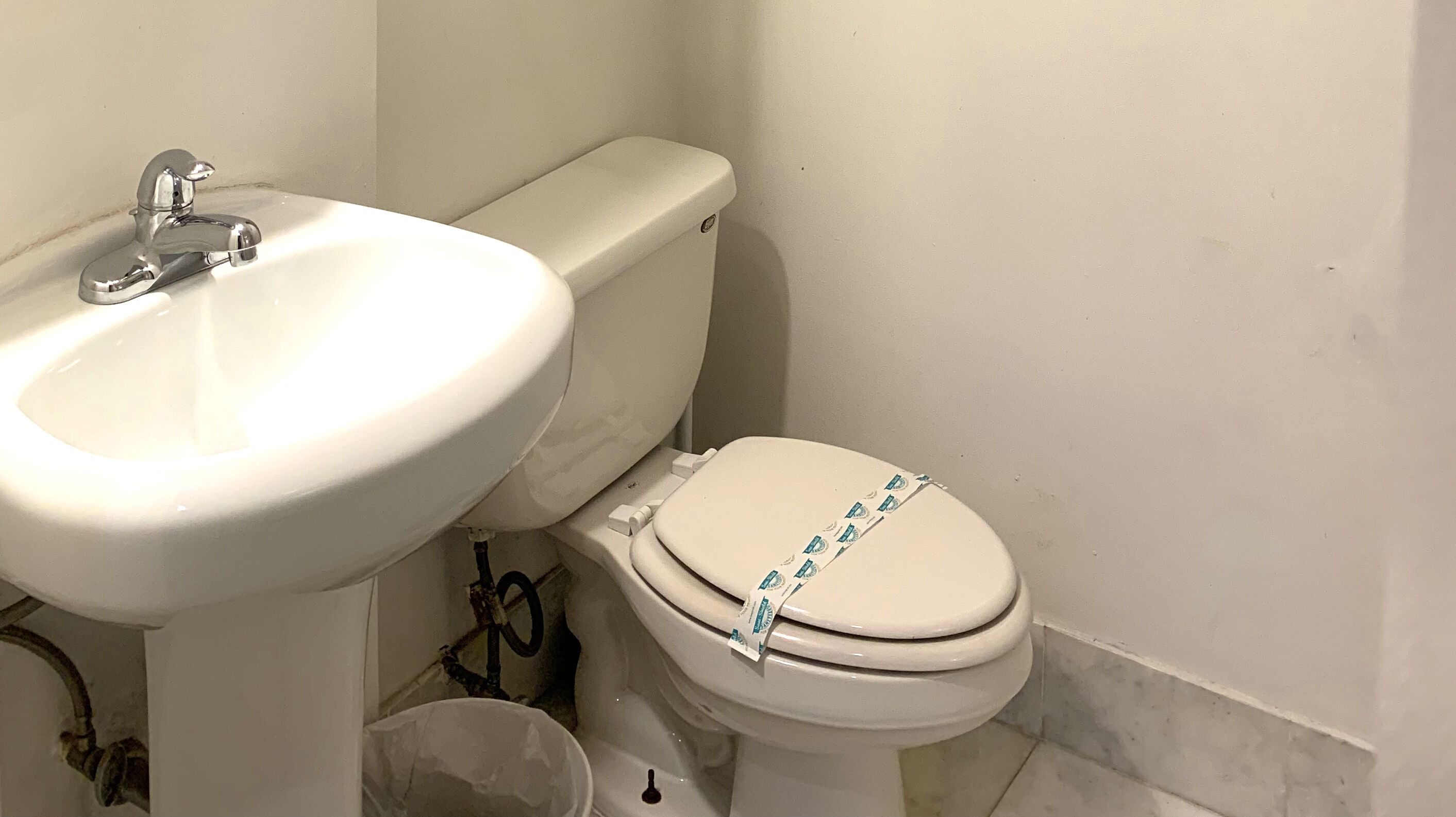 Ein Badezimmer mit weißem Waschbecken, Toilette und sichtbarer Sanitärinstallation.