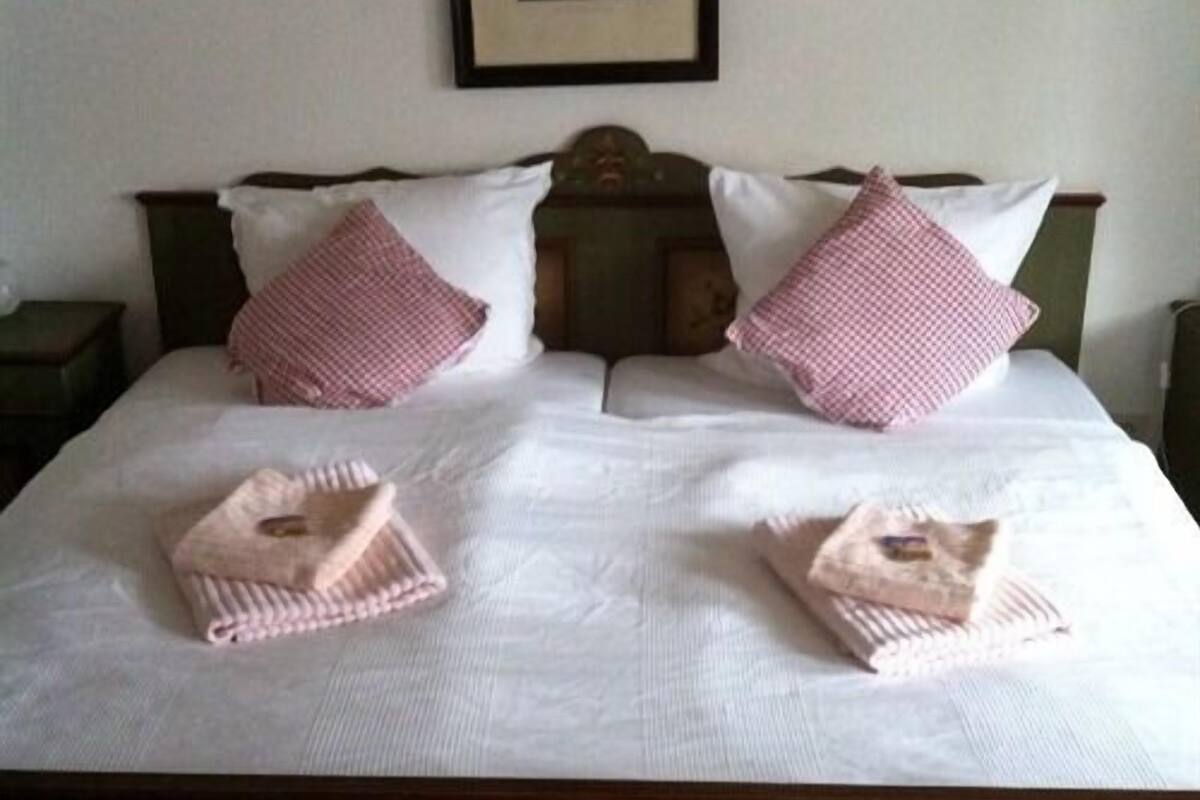A neatly made bed with white linens, two pink checkered pillows, and two folded towels.