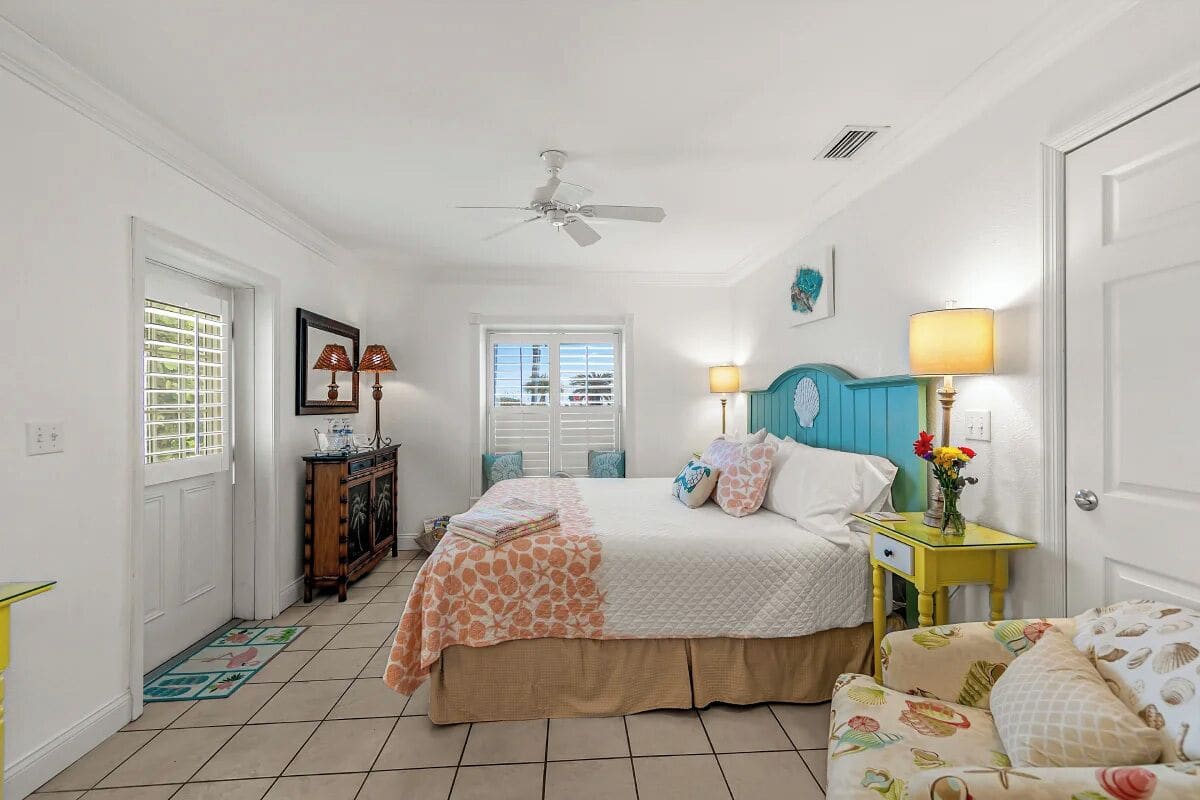 A bedroom with a bed, two bedside lamps, a ceiling fan, and a window with shutters.
