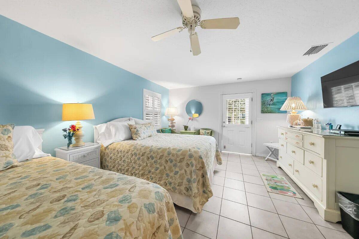 A bedroom with two beds, a ceiling fan, a dresser, and a window with blinds.