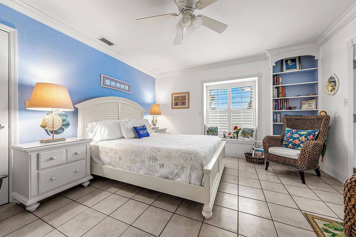 A bedroom with a bed, nightstands, a chair, a bookshelf, and a window with shutters.