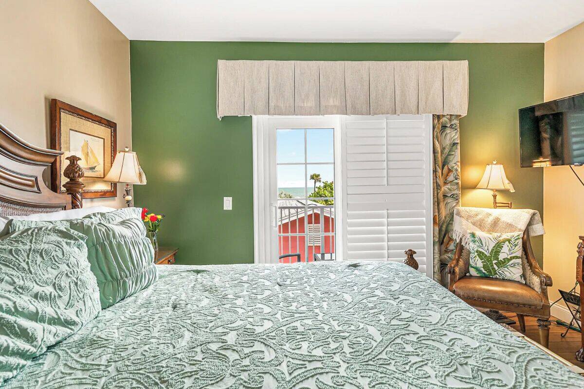 A bedroom with a large bed, a chair, a TV, and a window with shutters.