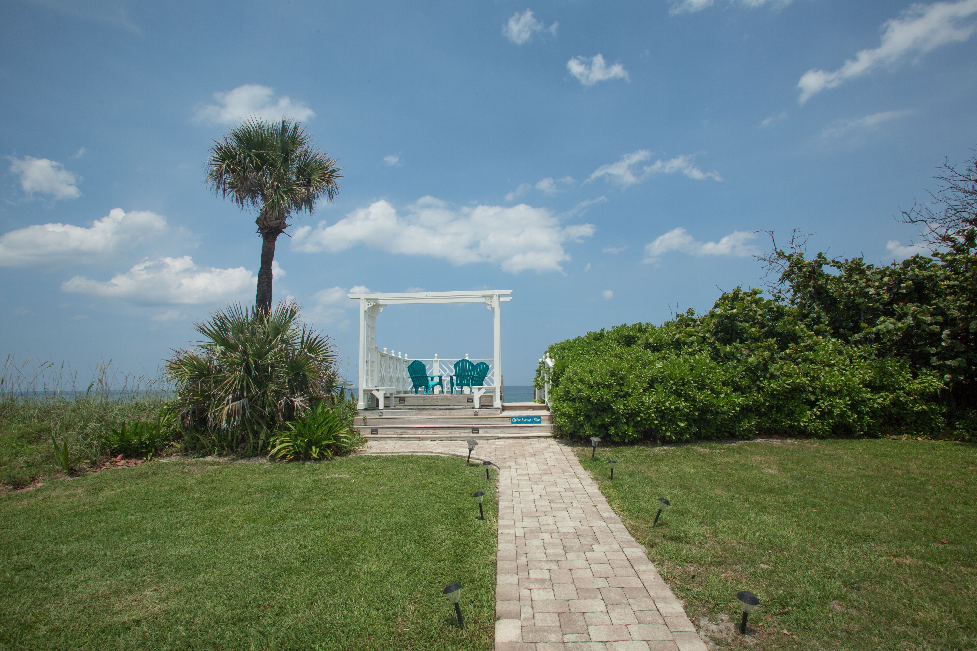 A white gazebo with green chairs and a small pool, surrounded by grass and plants.