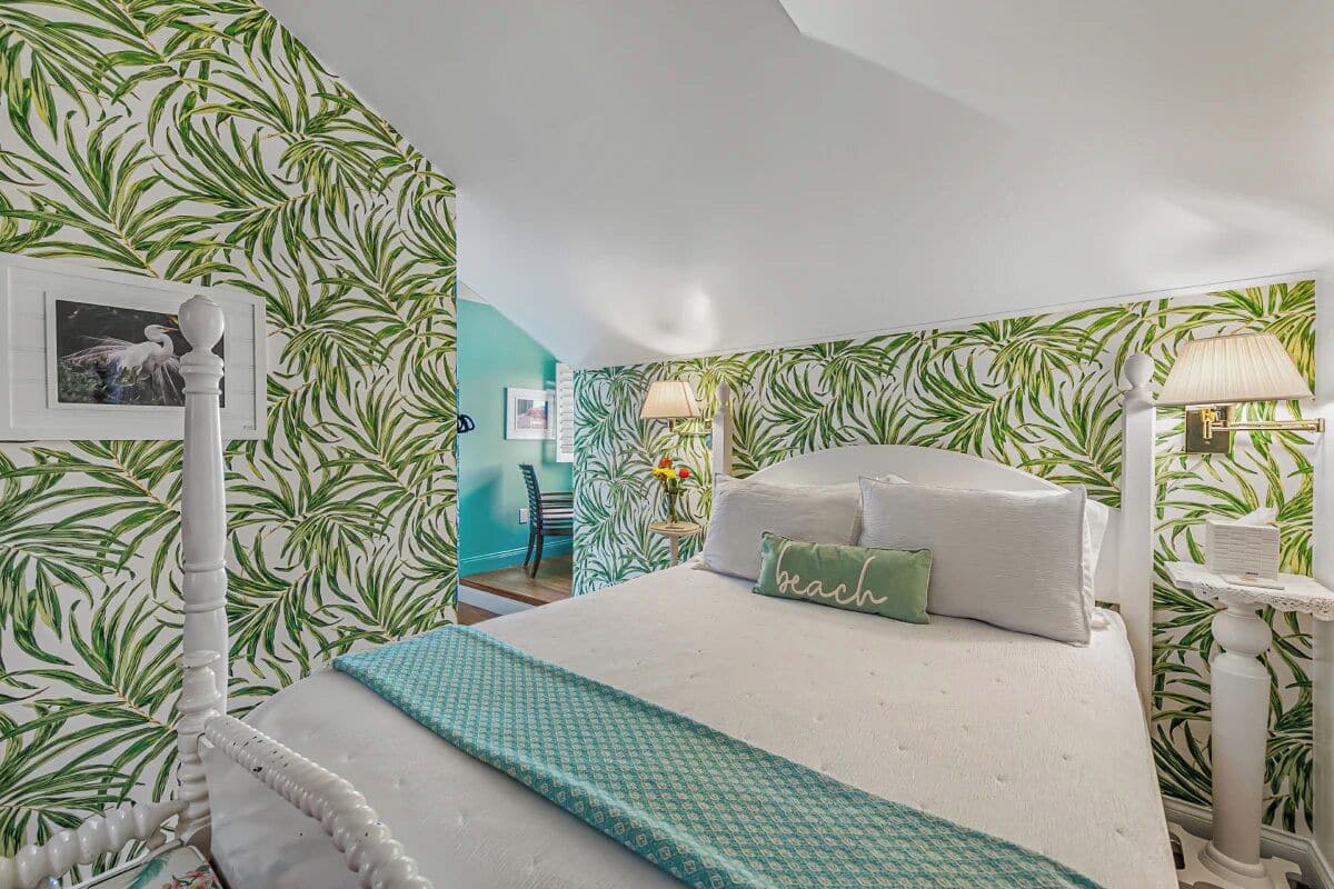 A bedroom with a bed, a nightstand, a lamp, and a wall with a tropical leaf pattern.