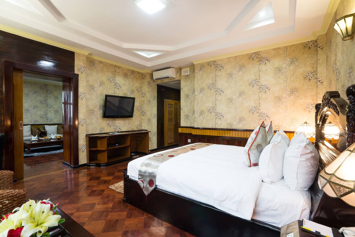 Ein Hotelzimmer mit einem großen Bett, einem Fernseher, einem Schreibtisch und einer dekorativen Lampe.