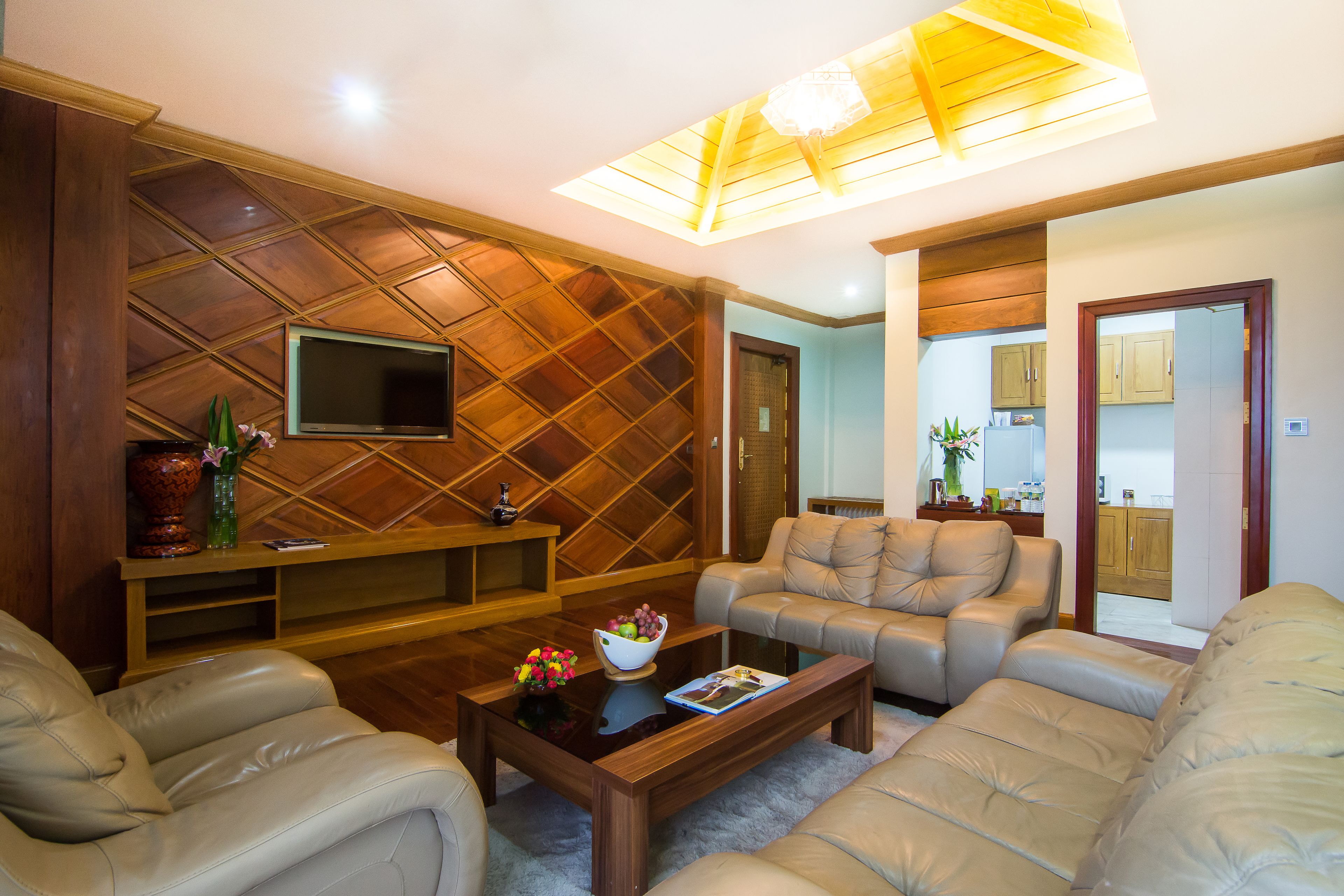 A living room with a wooden ceiling, a flat-screen TV, a coffee table with a bowl of fruit, and two sofas.