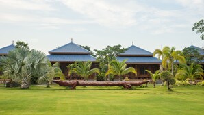 A traditional building with a blue roof, surrounded by lush greenery and palm trees. - Hotel Shwe Pyi Thar (Mandalay)