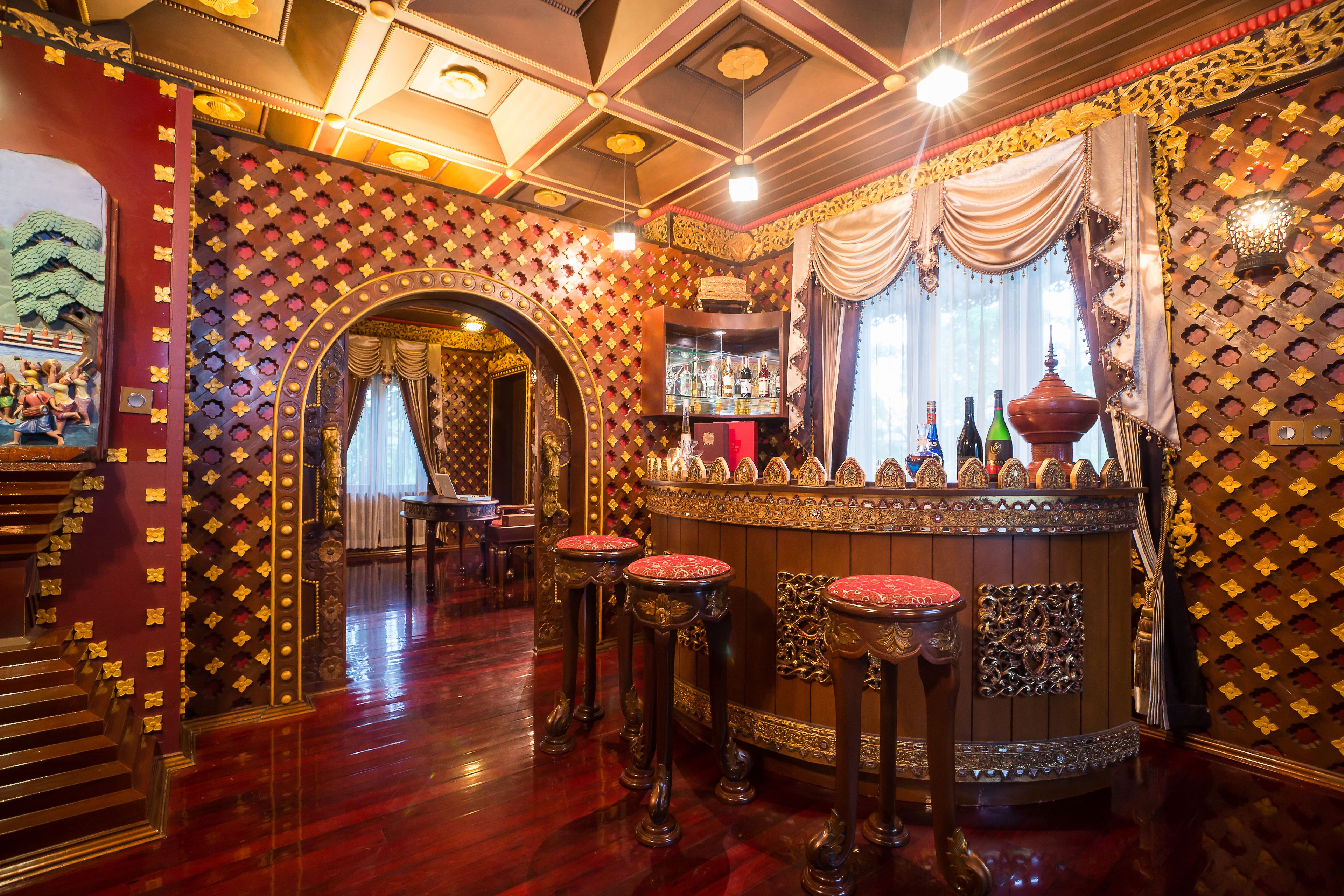 Una zona de bar con decoración elaborada, una barra con botellas y taburetes.