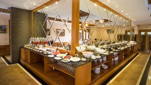 A buffet setup with various food items and beverages, wooden paneling, and a large mirror reflecting the room. - Hotel Shwe Pyi Thar (Mandalay)