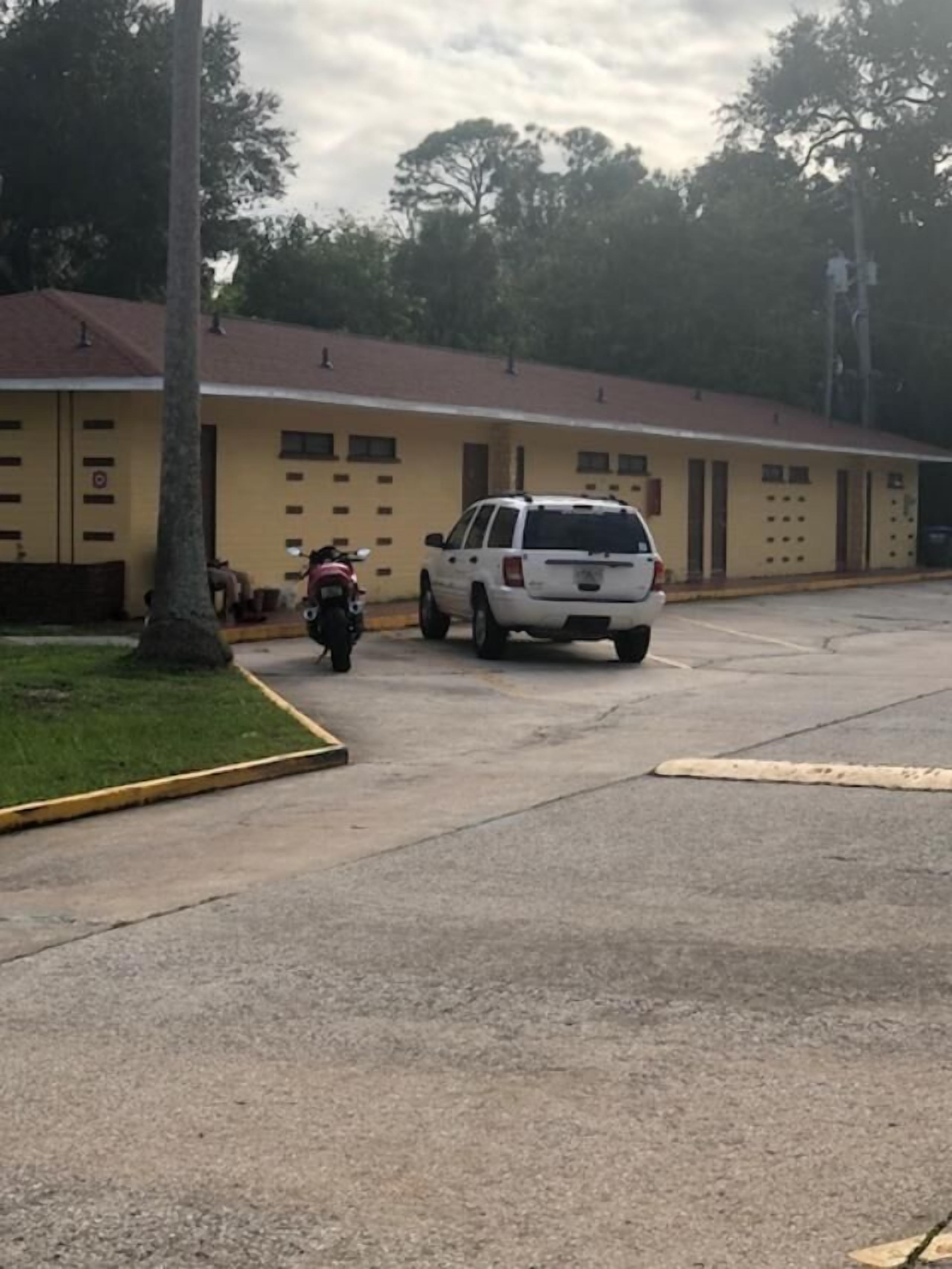 A building with a yellow facade, a parking lot, and a white SUV parked in front.